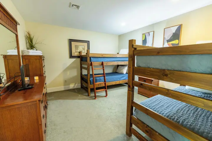 A room with bunk beds, a wooden dresser, a mirror, and a framed picture on the wall