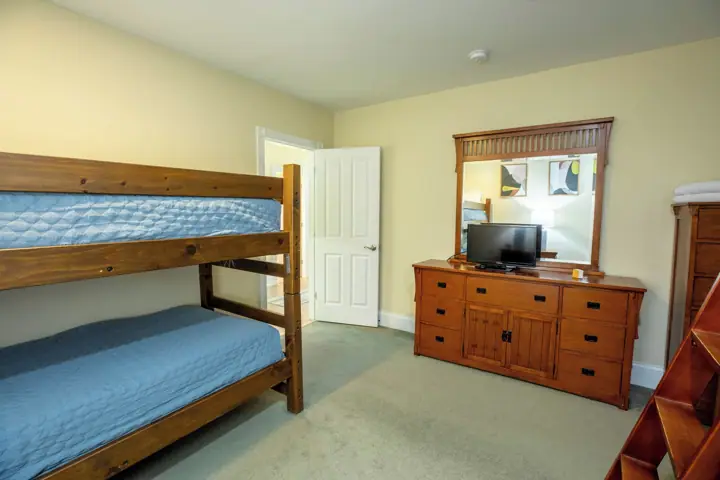 A room with bunk beds, a wooden dresser, a television, and a mirror