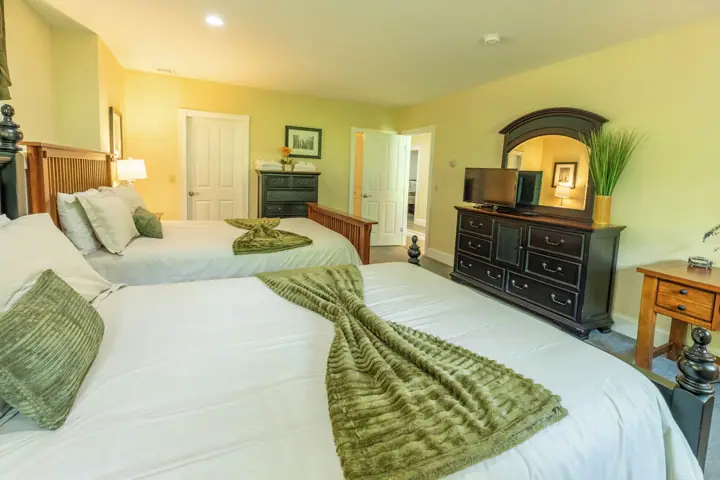 A hotel room with two beds, a dresser, a television, and a door leading to another room