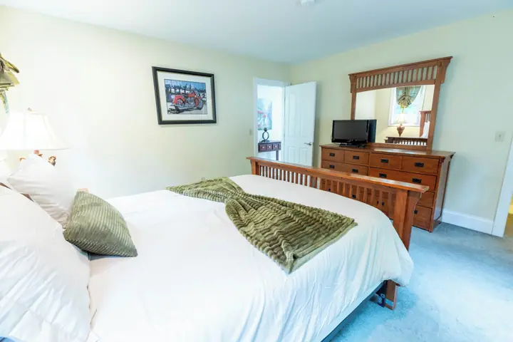 A bedroom with a bed, dresser, television, and a door leading to another room