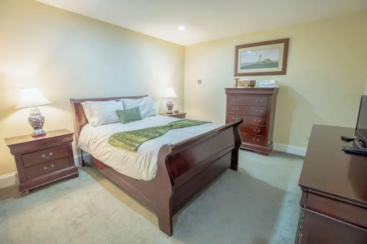 A bedroom with a wooden bed, two nightstands with lamps, a dresser, and a framed picture on the wall