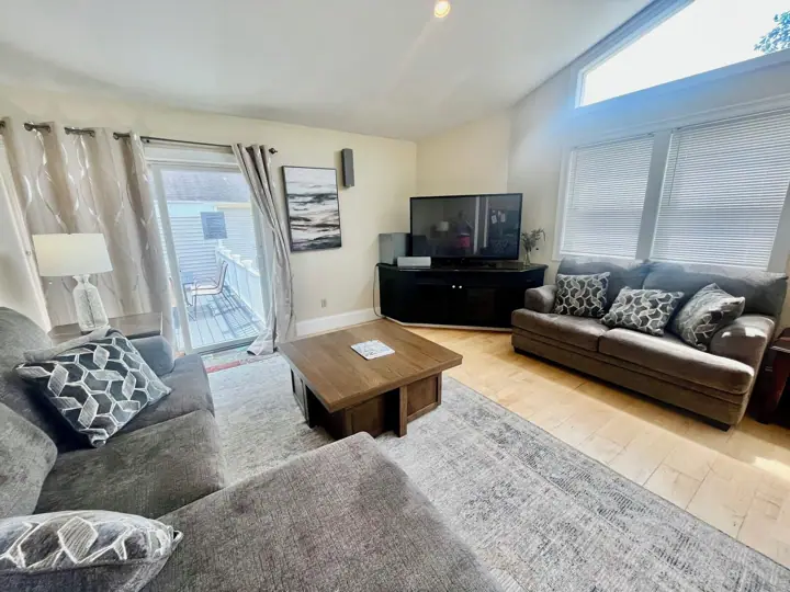 A living room with a sofa, coffee table, TV, and a view of the outside