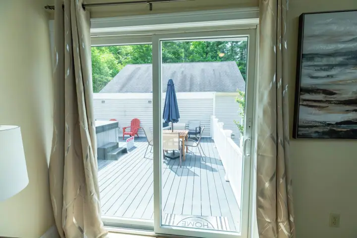 A sliding glass door leading to an outdoor deck with a table and chairs, a red chair, and a blue umbrella