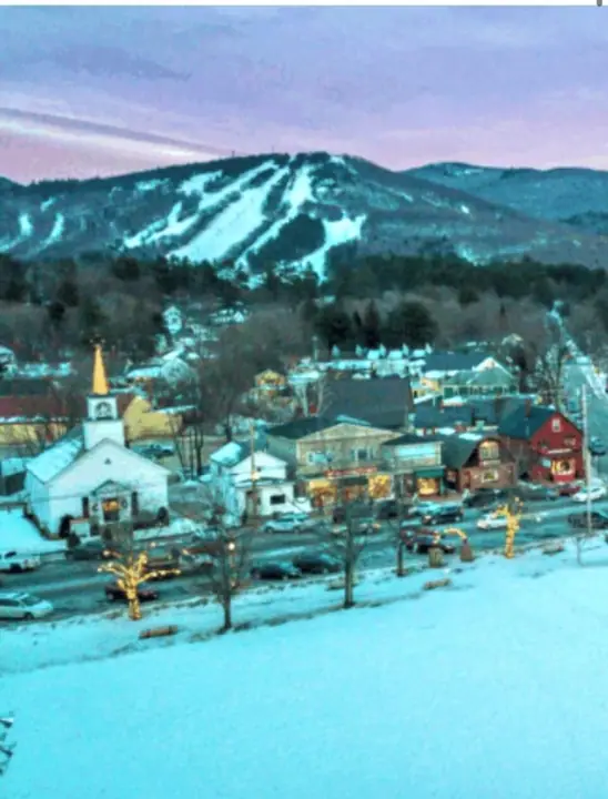 A town with buildings, a church, and snow-covered mountains in the background